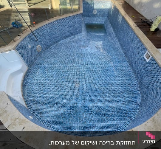 בריכה ריקה עם אריחים כחולים, ציוד תחזוקה בצד